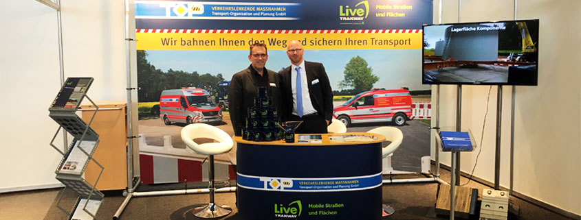 Geschäftsführer von TOP GmbH und Live Trakway auf dem Messestand in Offenburg, inklusive Messewand und Theke.